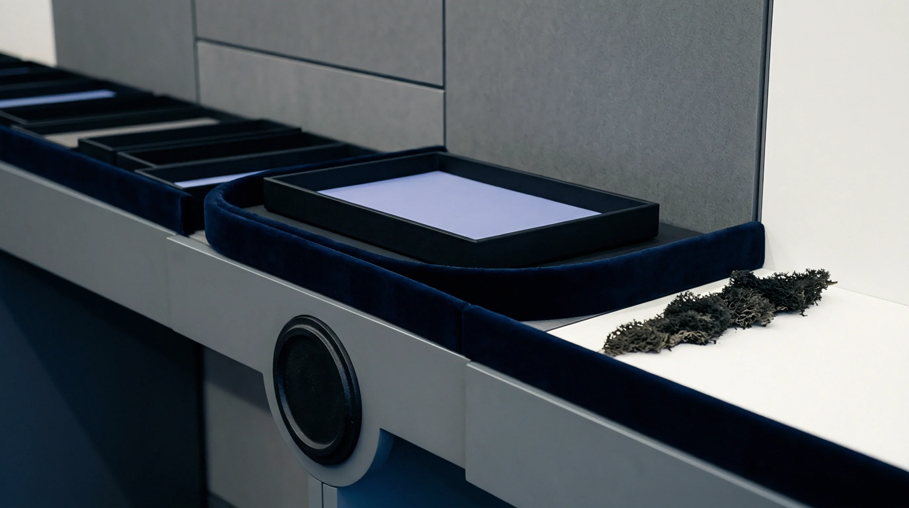 Modular grey merchandising fixtures feature dark blue velvet lined presentation trays alongside a raw organic specimen on a white surface.