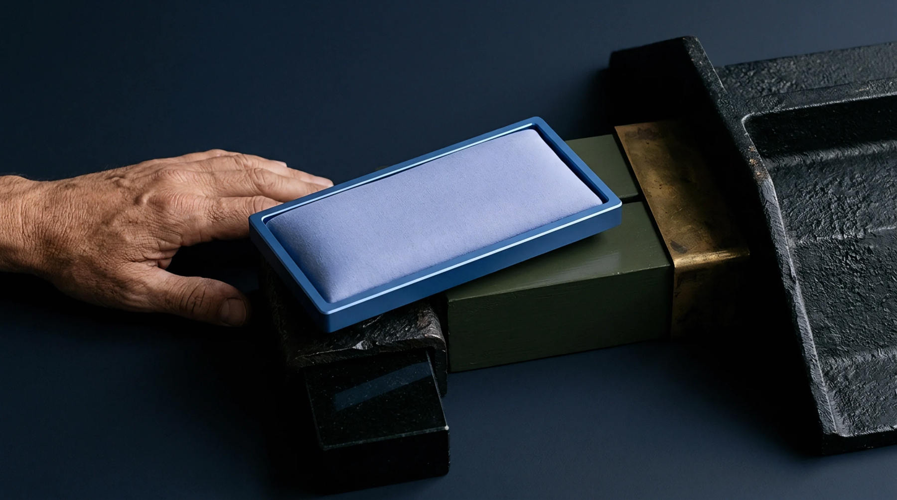 A rectangular blue tray with a lavender fabric cushion rests on green and black industrial prototyping blocks next to a hand.